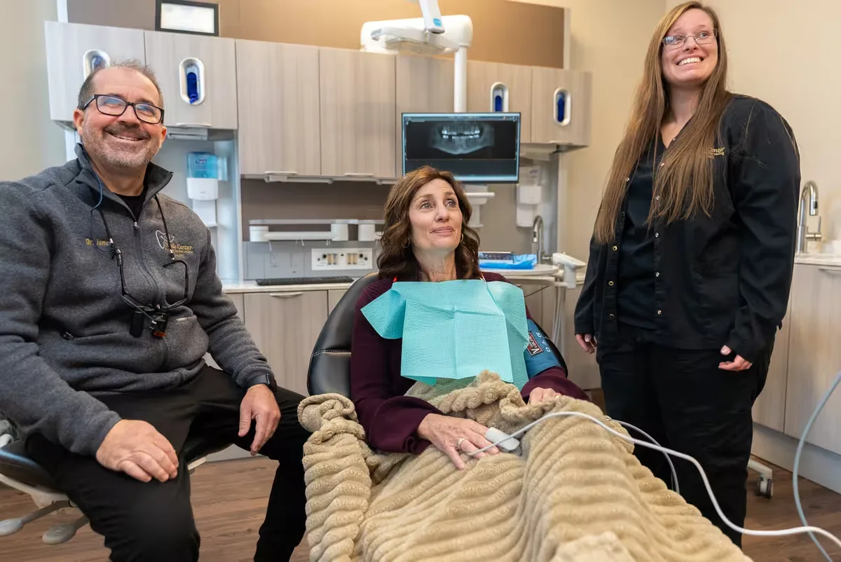 A relaxed patient resting under a comfort blanket while two Smile Center clinicians provide gentle care